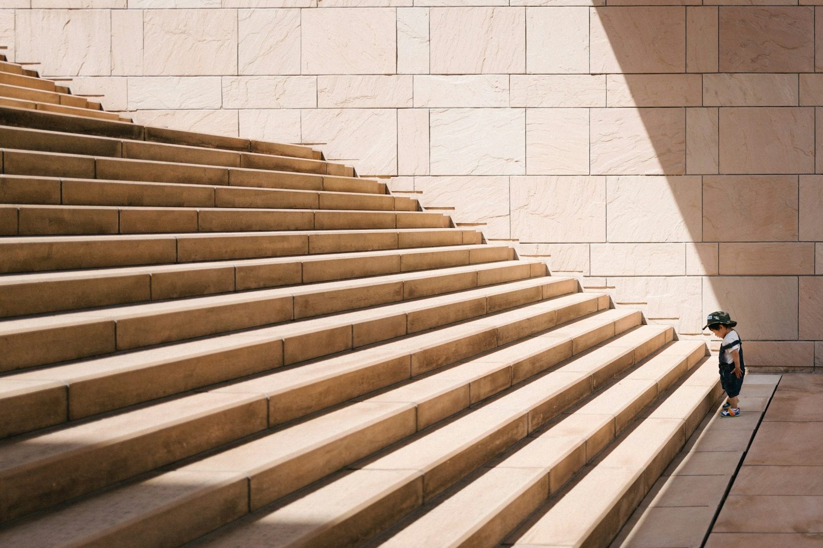 Coaching für persönliche Entwicklung: Kleines Kind im Schatten vor Treppe ins Licht – Symbol für Potenzial, Mut und individuelle Entfaltung.